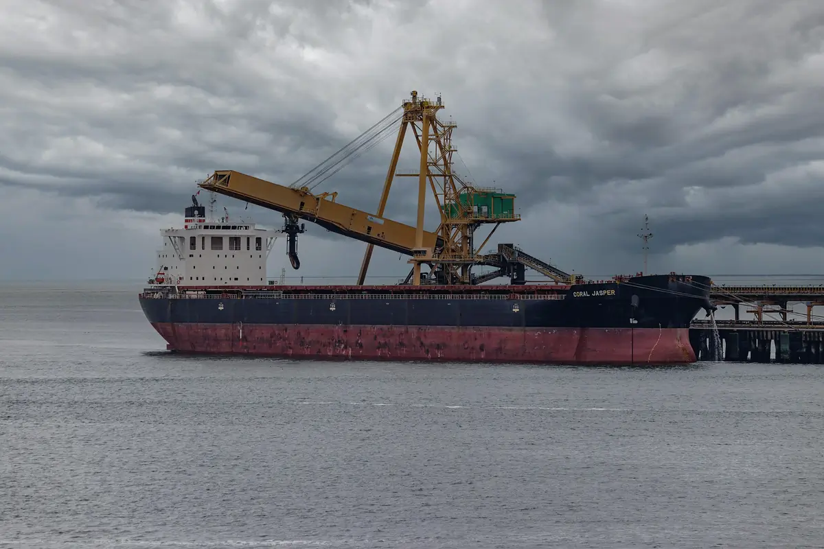 A bulk carrier alongside a loading conveyor under a stormy sky