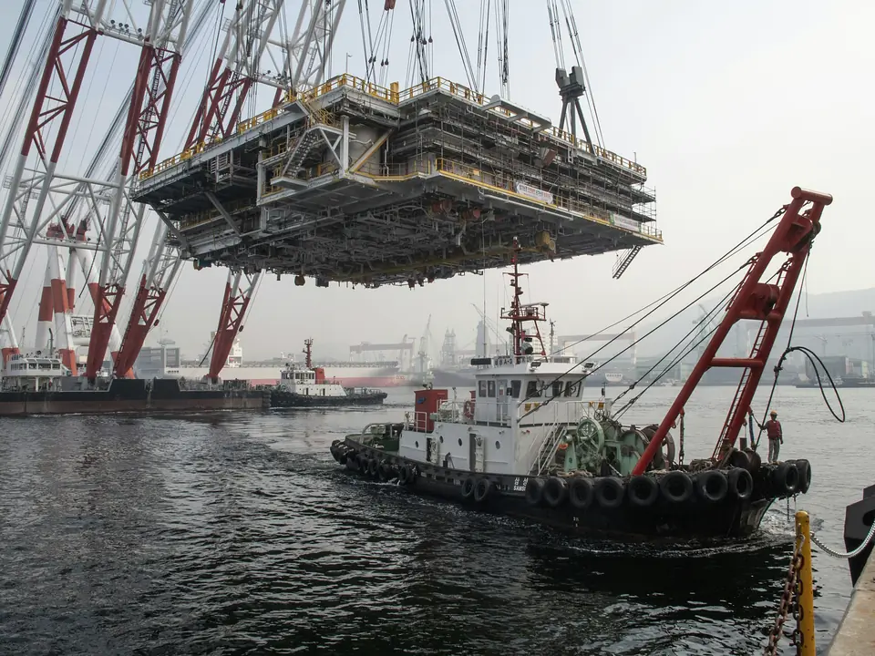 A floating crane lifting a large offshore module beside a tug