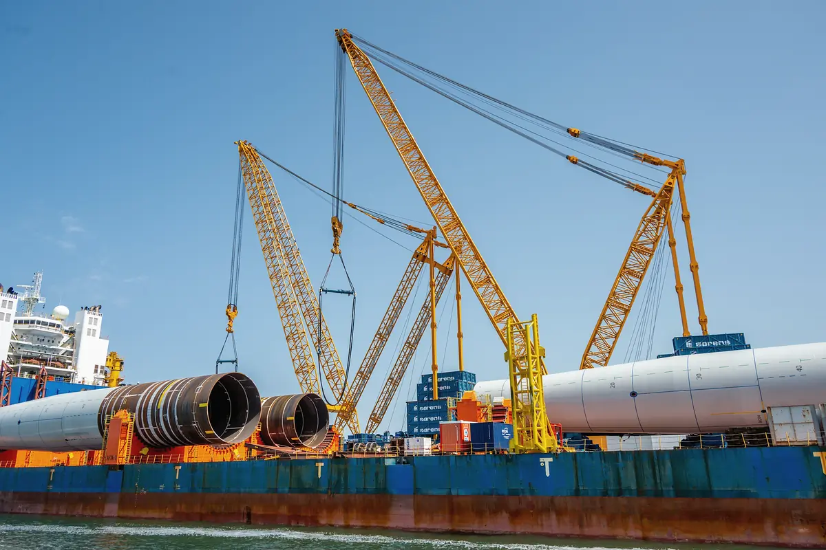 Cranes lifting large steel pipes onto a cargo ship